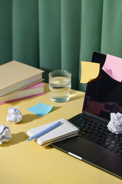A busy workspace featuring a laptop with sticky notes and pen