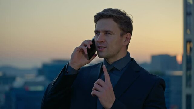 A Caucasian businessman leader encourages a partner during a phone conversation, making a number 1 gesture to promise success while on a rooftop in Seoul