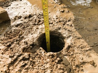 Depth measurement of soil hole using tape, great for construction, foundation, land survey, infrastructure projects, or geological survey concepts.