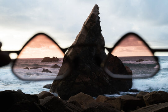 Hand holding glasses up against sea with rock 