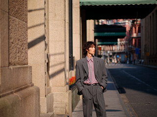 Portrait of handsome Chinese young man wearing gray suit posing in the street, young guy with black curly hair with urban background. Male fashion, cool Asian young man lifestyle.