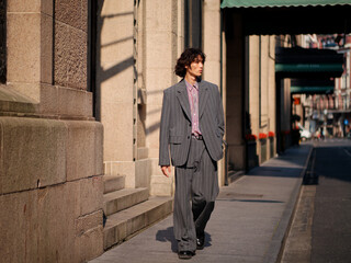 Portrait of handsome Chinese young man wearing gray suit walking in the street, young guy with black curly hair with urban background. Male fashion, cool Asian young man lifestyle.
