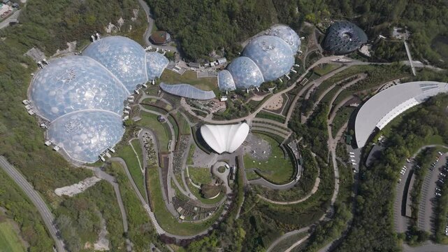 Expansive aerial panorama of Eden Project glass biomes nested in spiral gardens amid forested quarry, symbolising sustainable design, climate education and ecological diversity