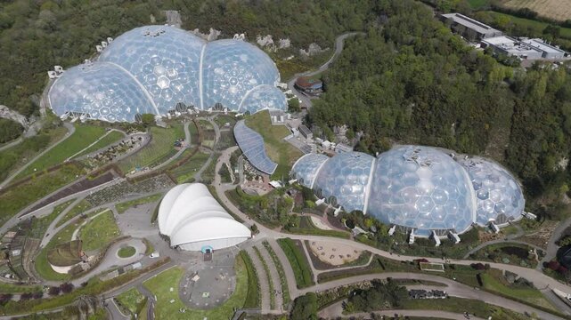 High-altitude view of Eden Project geodesic domes gleaming amid concentric botanical zones and wooded quarry slopes, emphasising innovative biomes and environmental stewardship