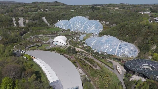 Panoramic aerial of interconnected Eden Project biomes sparkling above concentric botanical terraces and forested quarry walls, celebrating ecological education and climate innovation