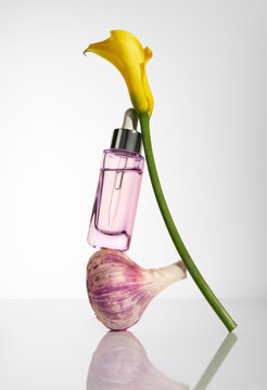 Still life with purple glass bottle of face serum, garlic and flower. 