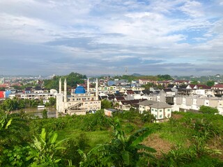 Fototapeta premium view of the city with mosque, houses and banana trees on a cloudy day