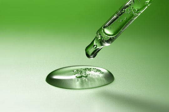 Glass pipette with anti-age moisturizing face serum on green backdrop - Powered by Adobe