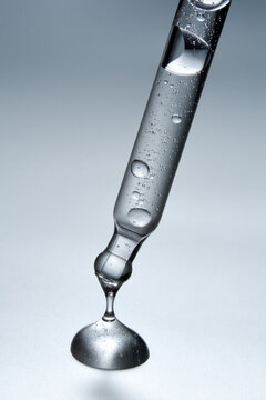 Clear glass pipette with a drop of cosmetic product falling down. 