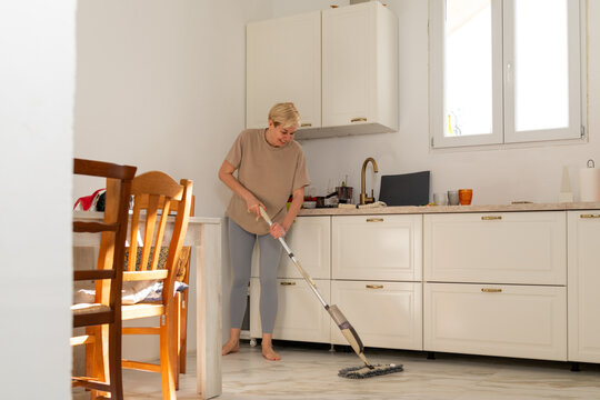 Female housewife cleaning floor with a mop in the kitchen