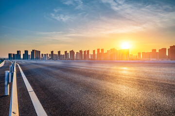 Empty asphalt highway road and modern city skyline with residential area buildings at sunset