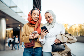 Two muslim businesswomen are walking and using their smartphones