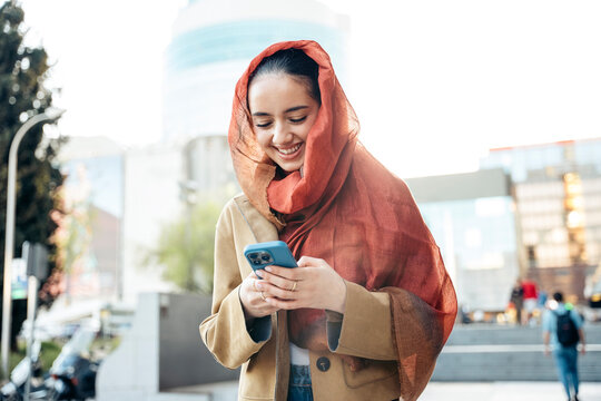 Smiling muslim woman wearing hijab using smartphone in urban setting