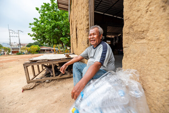 Elderly Thai man smiling in front of an abandoned house with collected