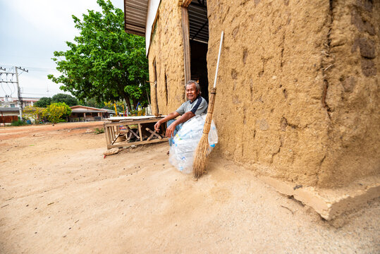 Elderly Thai man smiling in front of an abandoned house with collected