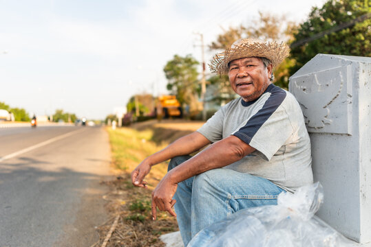 Elderly Thai man resting roadside with collected plastic bottles