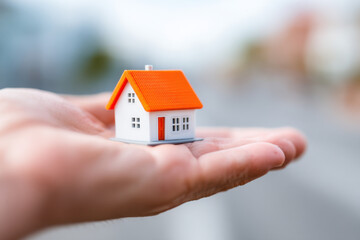 Hand holding a little house with an orange roof