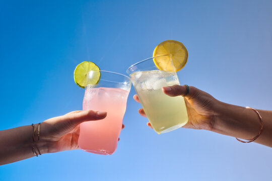 Two hands toasting with colorful, refreshing drinks under the sky