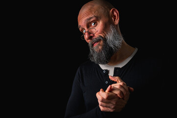 Funny bearded man with mischievous expression and clasped hands. Bald adult male posing on black...