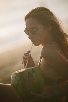 Woman Drinking Coconut Water on Tropical Beach at Sunset
