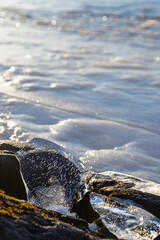 Close-up of a piece of transparent ice on a rock by a frozen lake on a sunny day in the winter. Focus on the foreground.