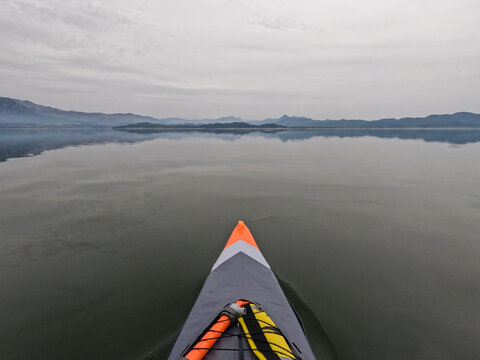 Paddling in a lake. POV. Grey and orange canoe on mirror like water