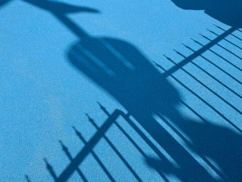 The shadow of a fence creates a pattern on a blue textured floor