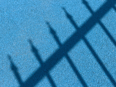 The shadow of a fence creates a pattern on a blue textured floor