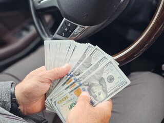 Handling a large amount of cash seated in a car showcasing the details of the bills and interior