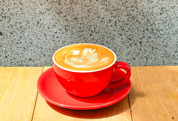 Close up view of hot cafe latte in the red cup. Wooden table, grey or gray wall as the background. Copy space. Coffee. Latte art. Dark, shadows, Black.