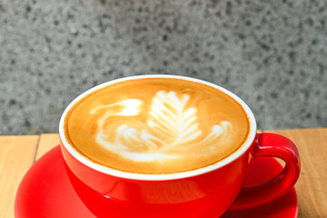 Extreme close up view of hot cafe latte in the red cup. Wooden table, grey or gray wall as the background. Copy space. Coffee. Latte art.