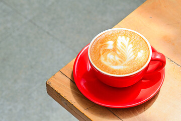 Close up view of hot cafe latte in the red cup. Wooden table, grey or gray floor, corner. Copy space. Coffee. Latte art. Dark, shadows.