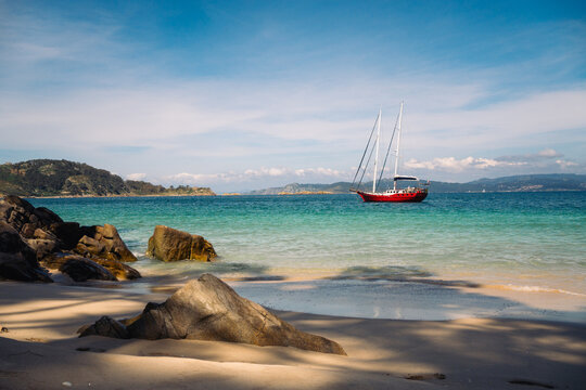 Red sailboat anchored in shallow turquoise water