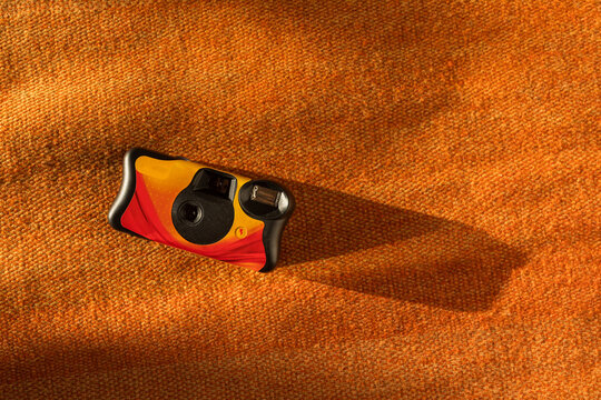 Film camera on orange fabric casting a long shadow