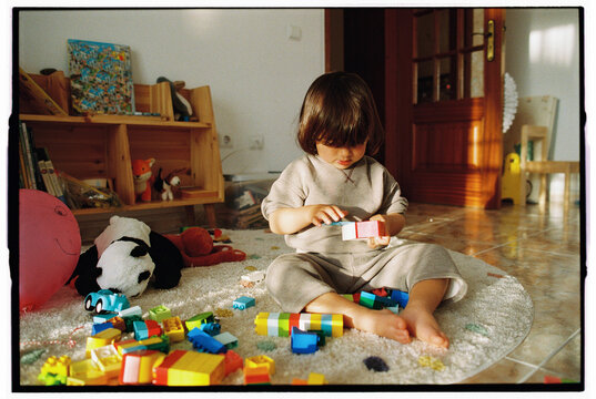 Child playing with building blocks on rug in toy-filled room