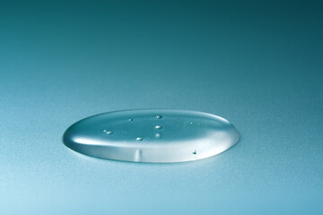 Droplet of fluid gel on cyan and blue gradient backdrop.