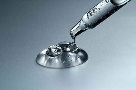 Clear glass pipette with a drop of cosmetic product falling down. 