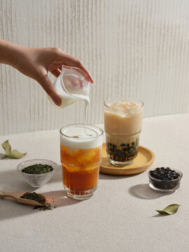 A hand pours milk into a glass of iced tea. Delicious bubble tea