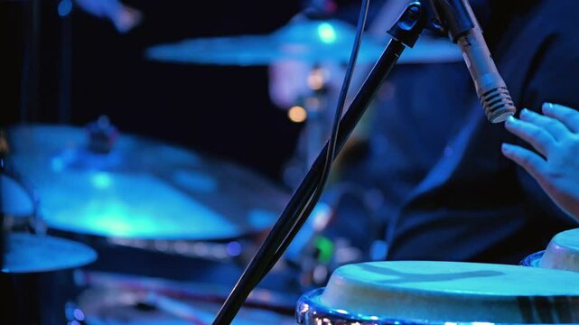 Close-up of a drummer playing the drums. In the foreground, a hand strikes a conga drum. Rhythm section of a jazz big band. Slow motion