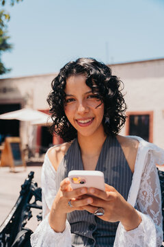 Hispanic woman using her cellphone at a downtown street.
