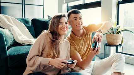 Obraz premium Competition, gamer couple and having fun in living room of home together for bonding or dating. Challenge, remote controller and video game with people in apartment for entertainment or relationship