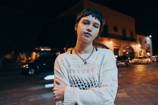 Confident non binary woman standing on the street at night.