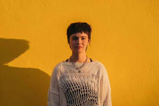 Non binary woman on a yellow wall background.