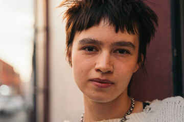 Non binary woman leaning against a door frame and looking at camera.