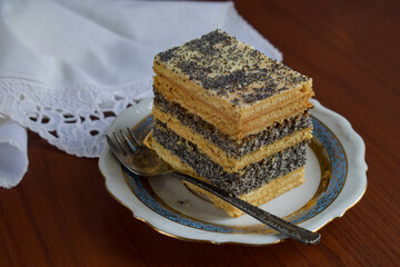 Layered poppy seed cake slice on porcelain plate with vintage spoon. Traditional homemade dessert, rustic style, festive baking, macro sweet food photography, close-up pastry on white background