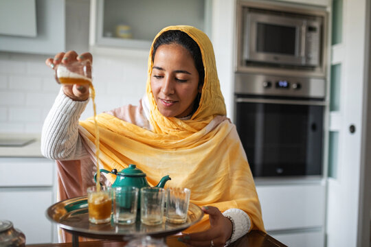 Arab woman in a yellow turban serving traditional tea.