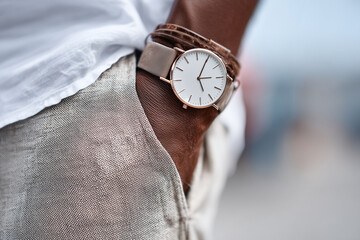 Close-up on man's wrist with simple analog watch and leather bracelet, hand in pocket of linen trousers, no visible brand, 