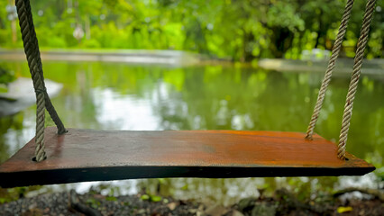 A close-up view of the swing shows its wooden seat smooth and quiet, hanging in front of a still pond bordered by the calm presence of trees.