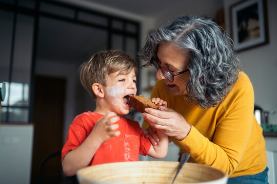 Grandmother giving grandson slice of cake in kitchen