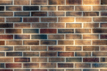 Abstract texture background of an exterior multi-shade reddish brown color vintage brick wall surface speckled with blue, in dappled sunlight from tree shadows